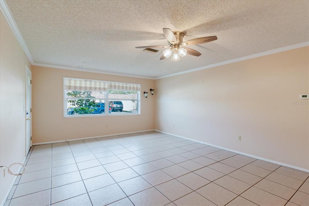 An empty room features light-colored tile flooring, beige walls, and a ceiling fan — 1201 CARA DRIVE, LARGO, FL
