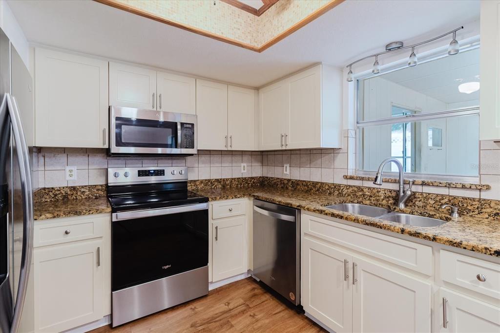 A kitchen features white cabinets, granite countertops, stainless steel appliances, and a window above the sink — 1201 CARA DRIVE, LARGO, FL