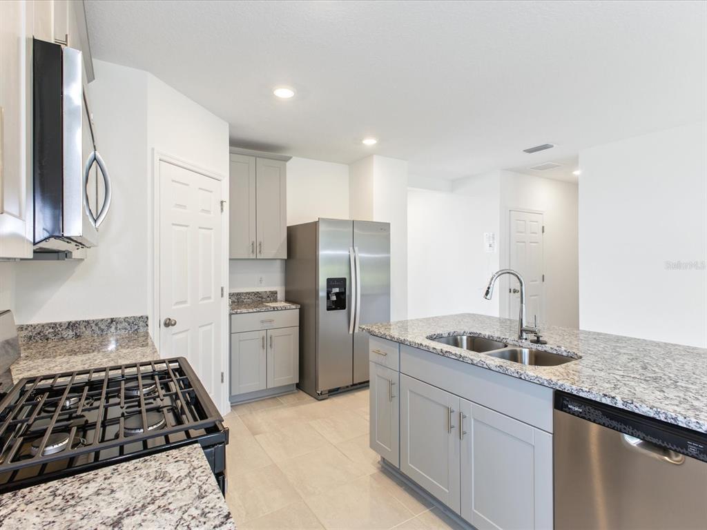 A kitchen features gray cabinets, granite countertops, stainless steel appliances, and a central island — 4542 EAGLE PERCH COURT, ST CLOUD, FL