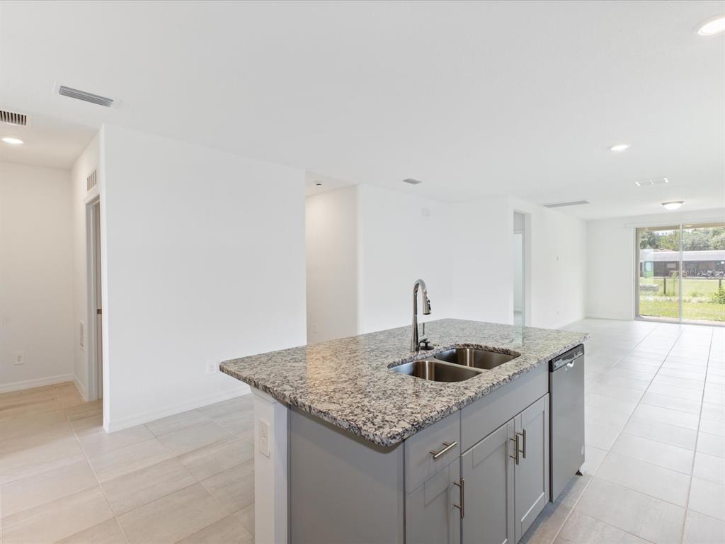A kitchen island with a granite countertop and gray cabinets sits in an open-concept room — 4542 EAGLE PERCH COURT, ST CLOUD, FL
