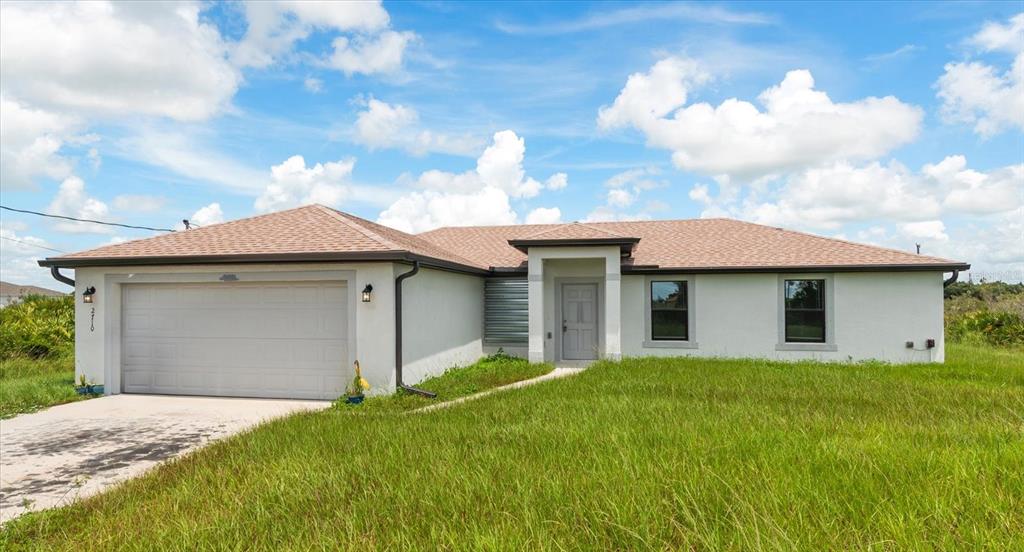 A single-story house with a white stucco exterior, a two-car garage, and a shingled roof — 2710 70TH STREET W, LEHIGH ACRES, FL