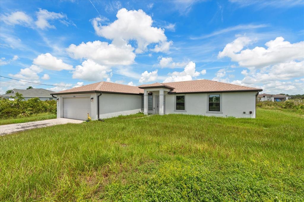 A single-story house with a white exterior, a two-car garage, and an overgrown grassy yard — 2710 70TH STREET W, LEHIGH ACRES, FL