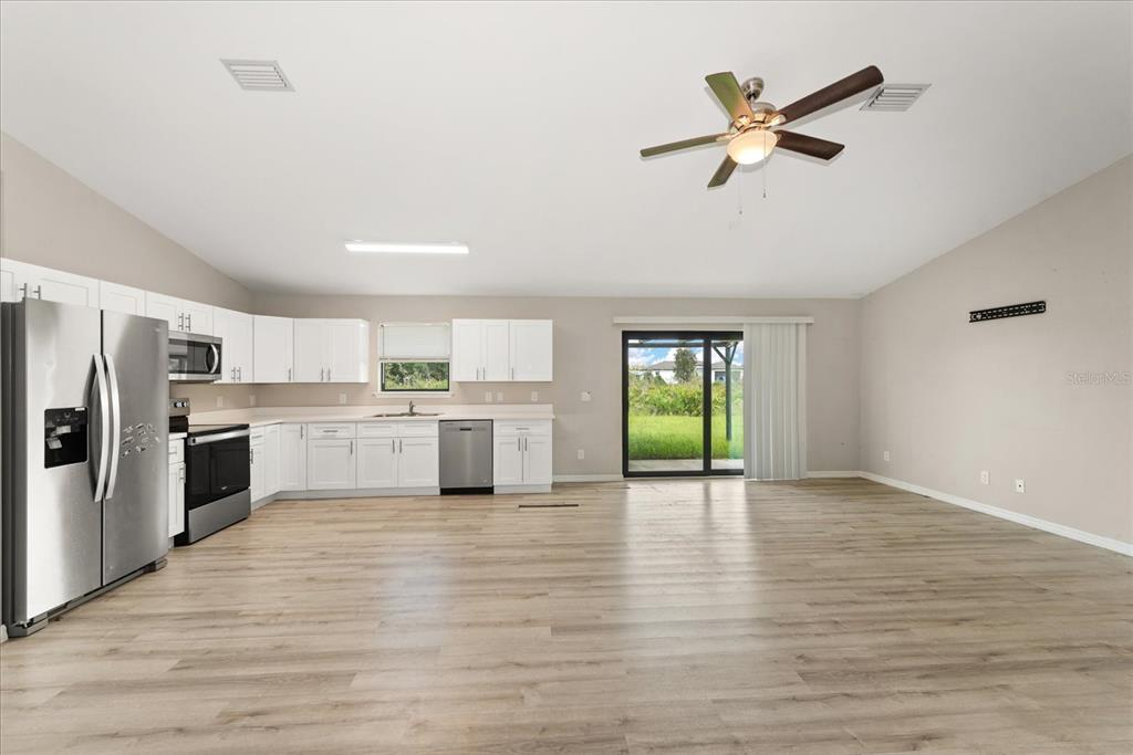 A kitchen with white cabinets and stainless steel appliances opens into a spacious living area — 2710 70TH STREET W, LEHIGH ACRES, FL