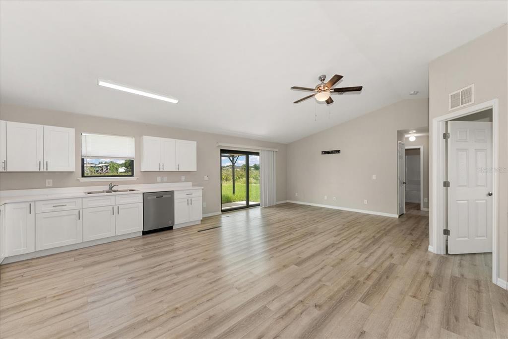 An open-concept kitchen and living area with white cabinets, light wood flooring, and sliding doors — 2710 70TH STREET W, LEHIGH ACRES, FL