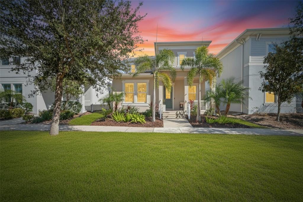 A two-story house with a front porch, palm trees, and a green lawn at sunset — 707 WINTERSIDE DRIVE, APOLLO BEACH, FL