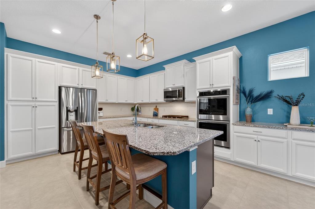 A kitchen features white cabinetry, granite countertops, a teal island, and stainless steel appliances — 707 WINTERSIDE DRIVE, APOLLO BEACH, FL
