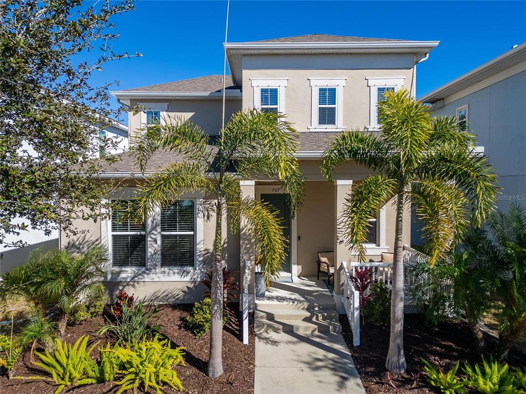 A two-story house with a tan exterior, palm trees, and a front porch entrance — 707 WINTERSIDE DRIVE, APOLLO BEACH, FL