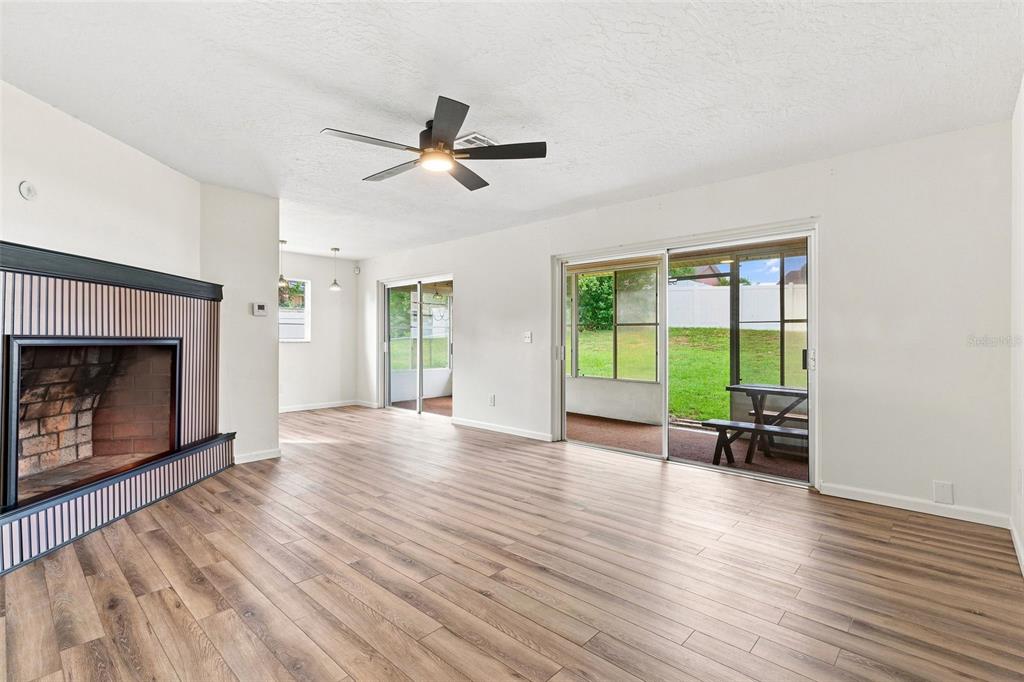 A living room features light wood-look flooring, a brick fireplace, and sliding glass patio doors — 1441 NE OLD MILL DRIVE, DELTONA, FL