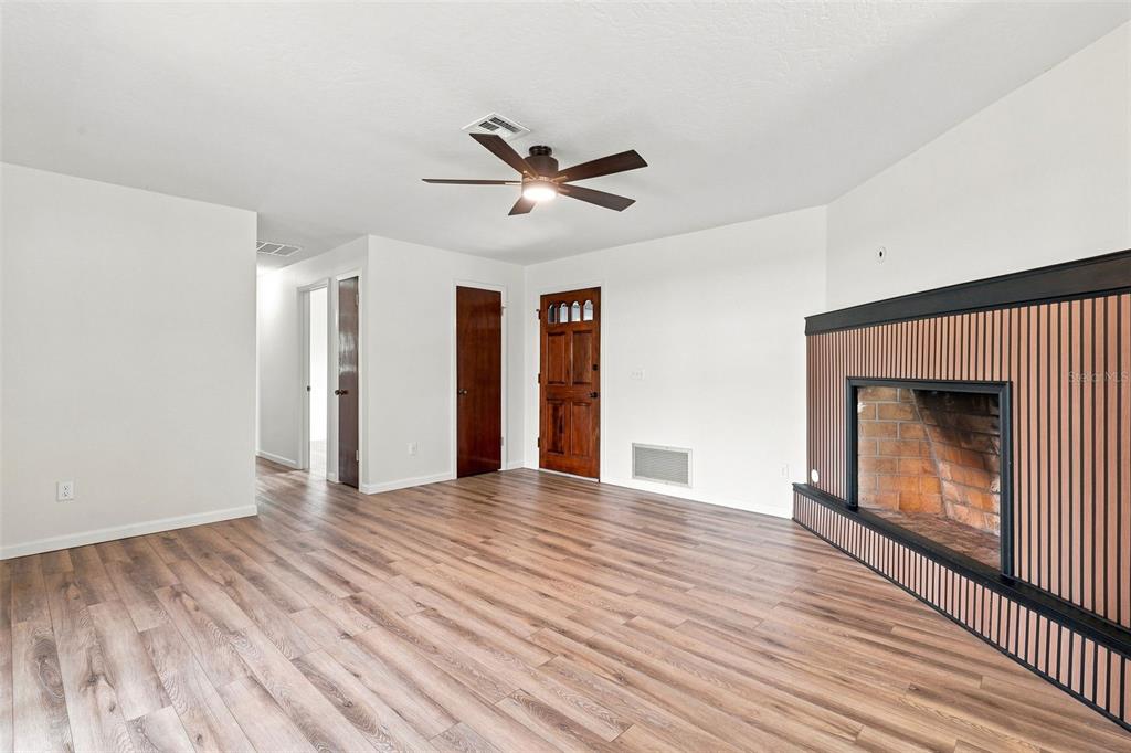 A living room features wood-look flooring, a ceiling fan, and a fireplace with wood paneling — 1441 NE OLD MILL DRIVE, DELTONA, FL