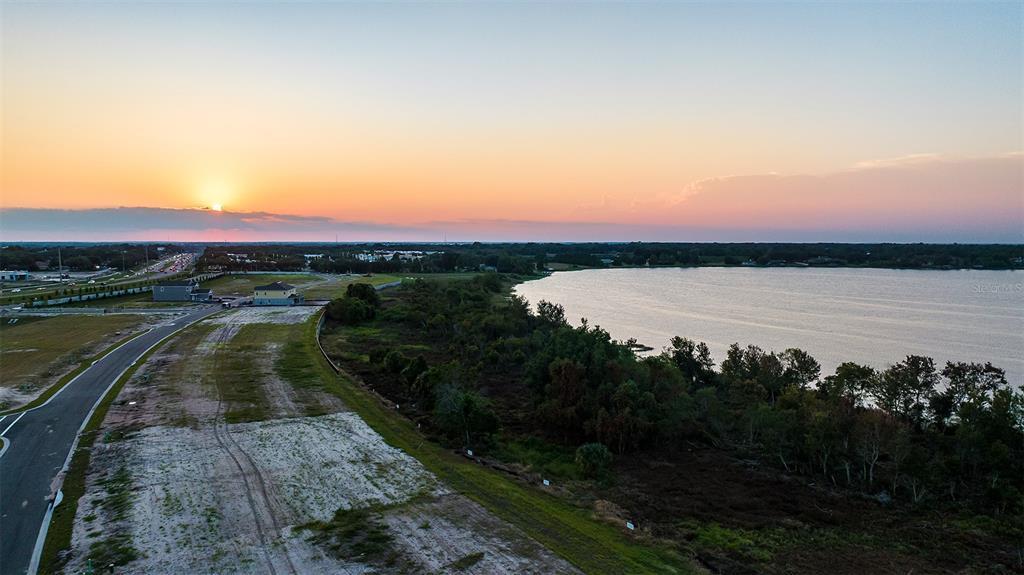 An aerial view shows a sunset over a lake next to a developing residential area — 19341 LOCHSIDE LANE, MOUNT DORA, FL