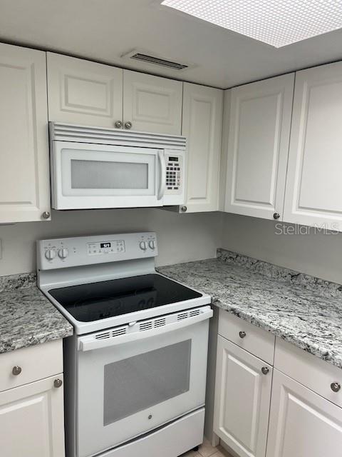 A kitchen features white cabinets, a white microwave, a white electric stove, and granite countertops — 452 BANYON TREE CIRCLE UNIT 200, MAITLAND, FL