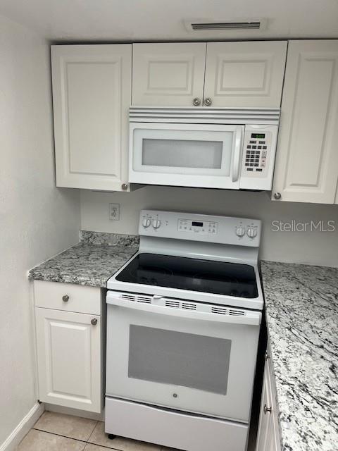 A kitchen features white cabinets, a white microwave, a white electric range, and granite countertops — 452 BANYON TREE CIRCLE UNIT 200, MAITLAND, FL