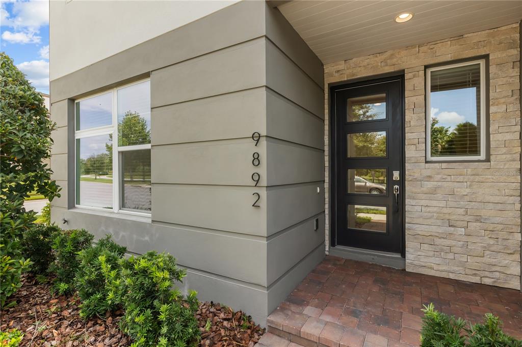 A modern home entrance features a black front door, stone siding, and vertical house numbers — 9892 BUCKLOW HILL DRIVE, ORLANDO, FL