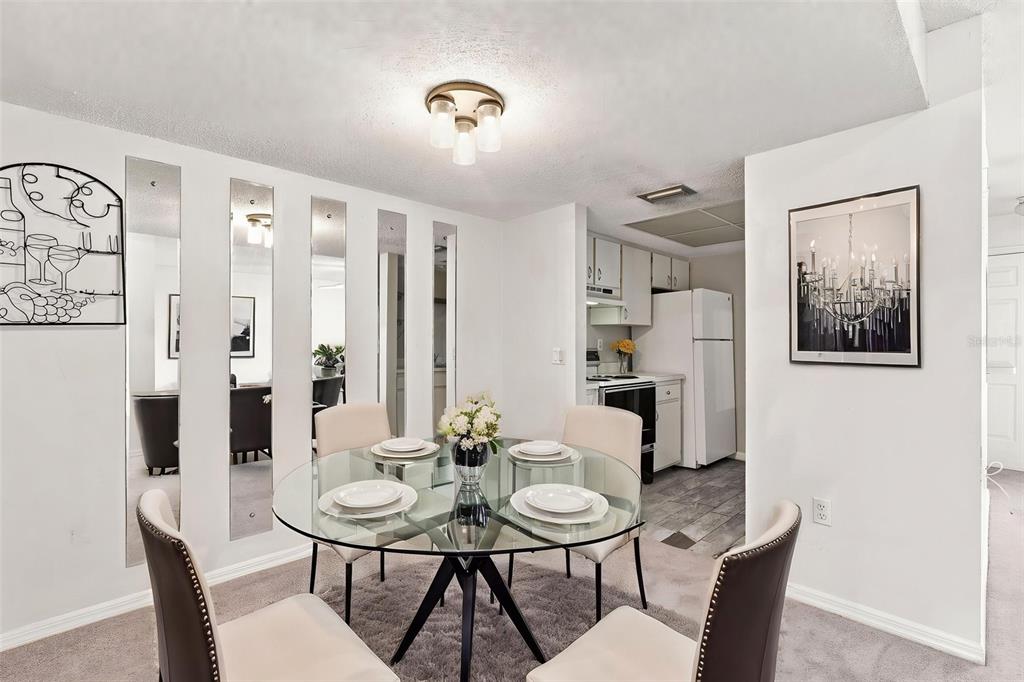 A dining area features a glass-topped table, four chairs, mirrored wall panels, and an adjacent kitchen — 22278 VICK STREET UNIT A101, PORT CHARLOTTE, FL