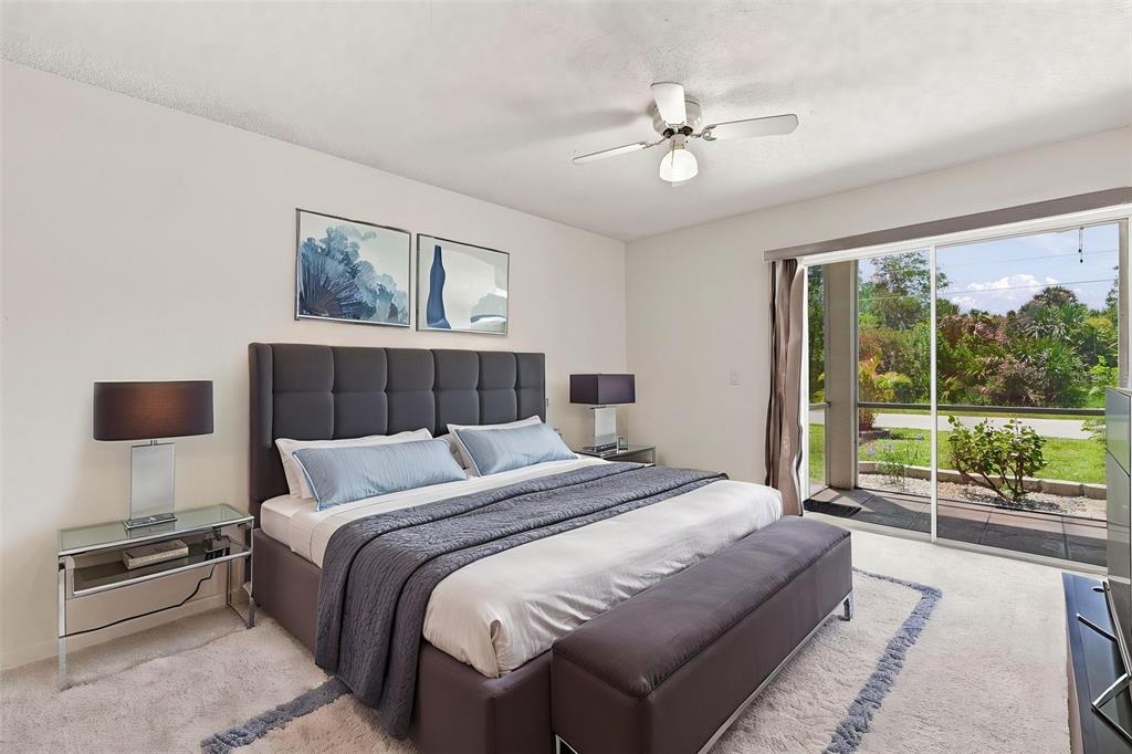 A bedroom features a gray upholstered bed, matching bench, glass nightstands, and a sliding glass door — 22278 VICK STREET UNIT A101, PORT CHARLOTTE, FL