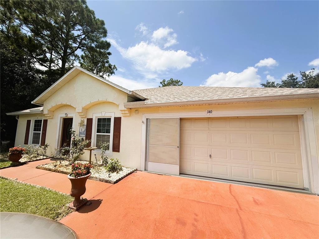 A single-story house with a beige stucco exterior, brown shutters, and a two-car garage — 140 PERSIMMON DRIVE, PALM COAST, FL