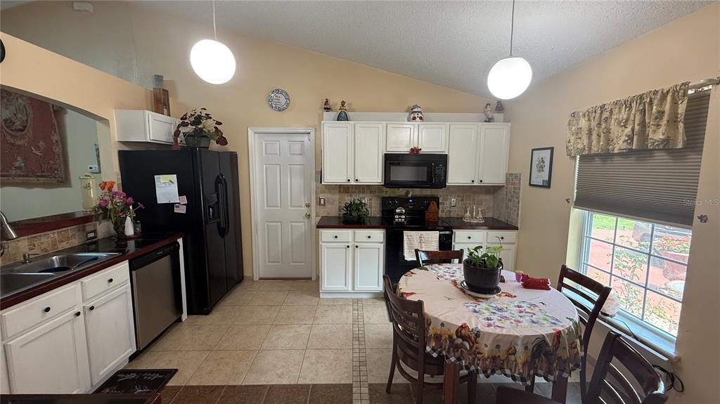 A kitchen features white cabinets, black appliances, a dining table, and tile flooring — 140 PERSIMMON DRIVE, PALM COAST, FL