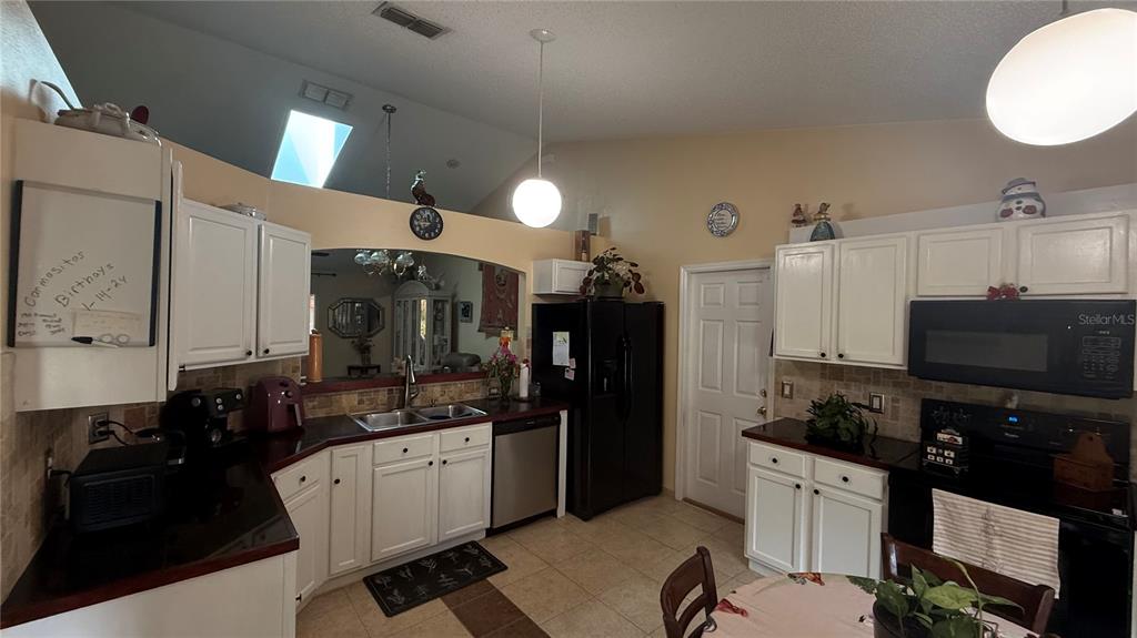 A kitchen features white cabinets, dark countertops, a black refrigerator, and a vaulted ceiling — 140 PERSIMMON DRIVE, PALM COAST, FL