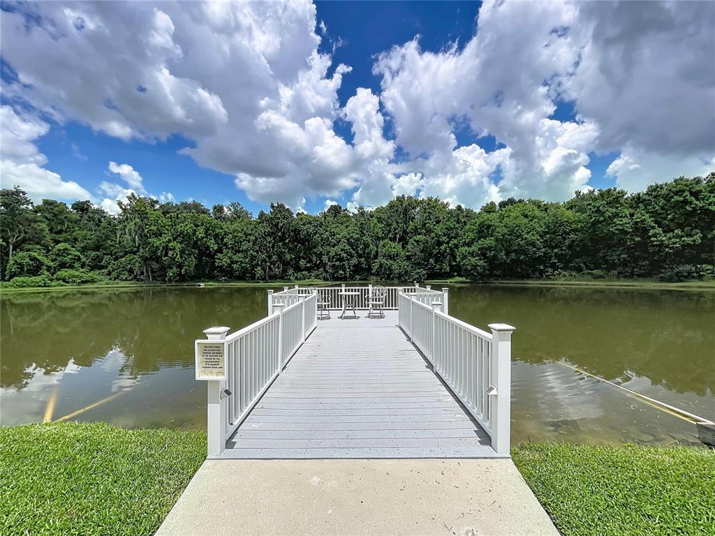 A wooden dock with white railings extends over a calm pond toward a wooded area — 4983 PLEASANT HOLLOW TRAIL, LAKELAND, FL
