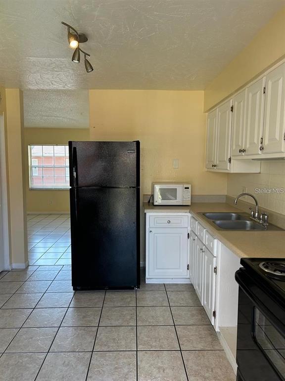 A kitchen features white cabinets, a black refrigerator, a microwave, and light-colored tile flooring — 1627 W OAK RIDGE ROAD UNIT D, ORLANDO, FL