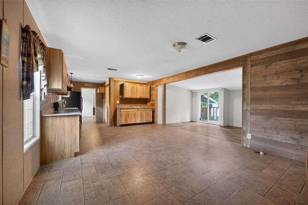 An open-concept kitchen and living area feature tile flooring and wood-paneled accent walls — 4389 288TH TERRACE, BRANFORD, FL