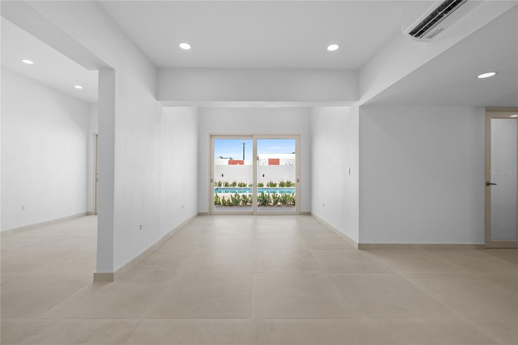 A bright, minimalist room with white walls, large floor tiles, and sliding doors to a pool — E 10 CALLE MADRE PERLA, DORADO, PR