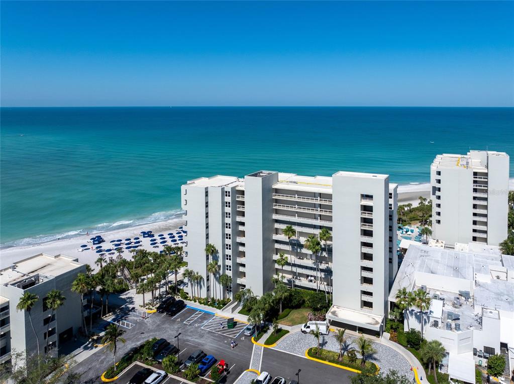 An aerial view shows a multi-story beachfront condominium complex with a parking lot and beach — 210 SANDS POINT ROAD UNIT 2101, LONGBOAT KEY, FL