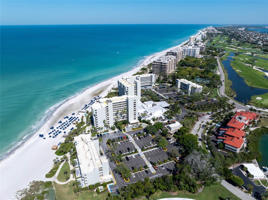 An aerial view shows beachfront high-rise condominiums, a parking lot, and a nearby golf course — 210 SANDS POINT ROAD UNIT 2101, LONGBOAT KEY, FL