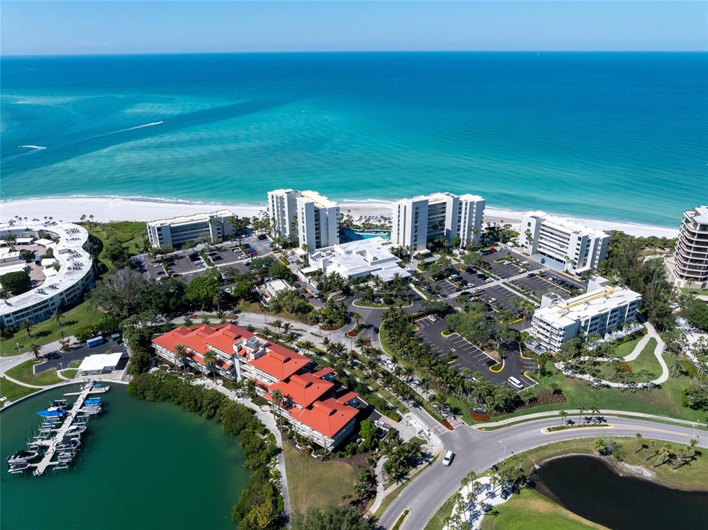 An aerial view shows a coastal resort complex with multiple buildings, parking lots, and a marina — 210 SANDS POINT ROAD UNIT 2101, LONGBOAT KEY, FL