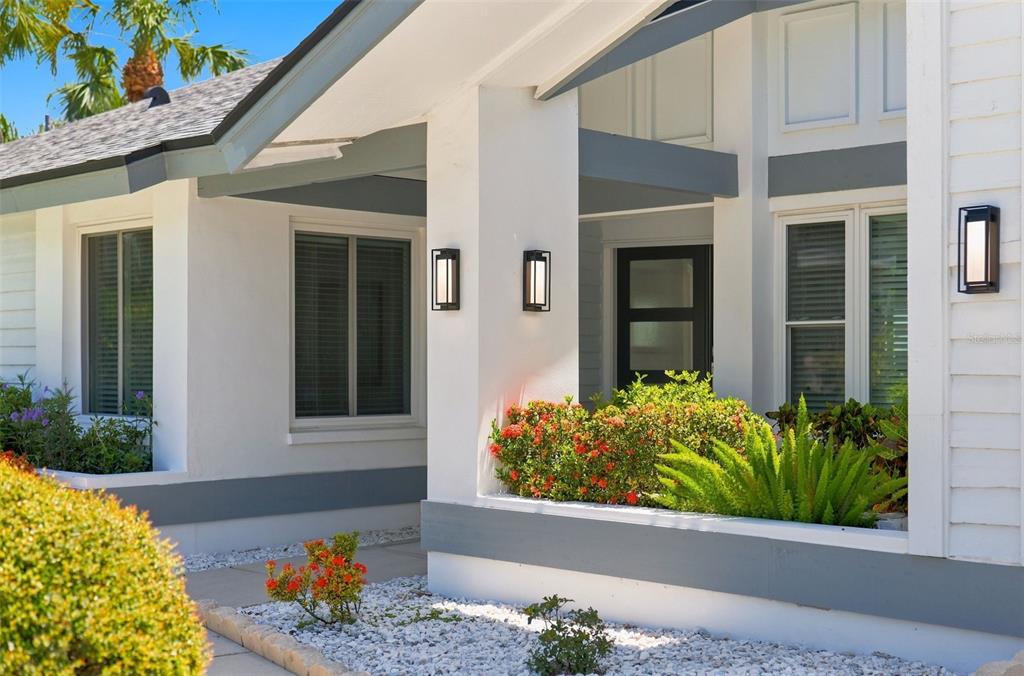 A modern house exterior features white walls, gray trim, black light fixtures, and landscaped garden beds — 5921 SEABIRD DRIVE S, GULFPORT, FL