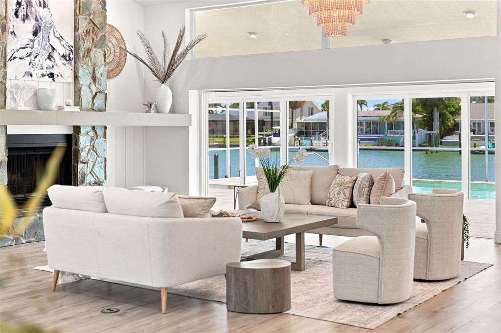A living room with a stone fireplace, neutral furniture, and large sliding doors overlooking a canal — 5921 SEABIRD DRIVE S, GULFPORT, FL