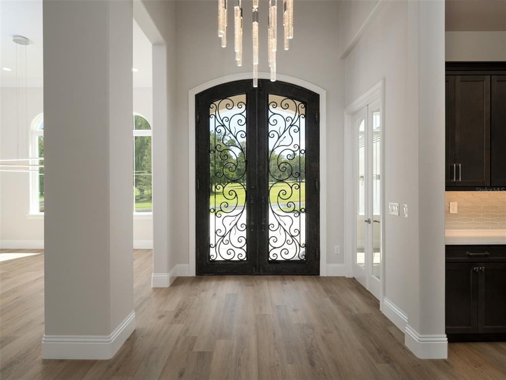 An entryway features light wood flooring, a modern chandelier, and a decorative iron double door — 7647 NW 33RD PLACE, OCALA, FL