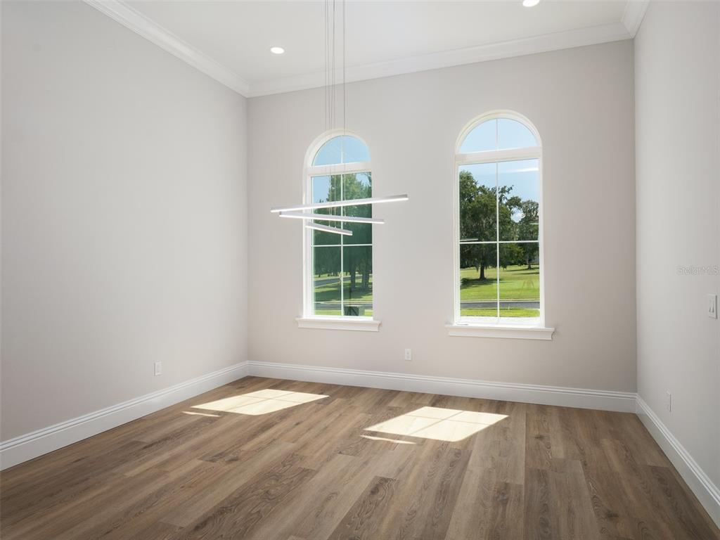 An empty room features light wood flooring, two arched windows, and a modern linear chandelier — 7647 NW 33RD PLACE, OCALA, FL