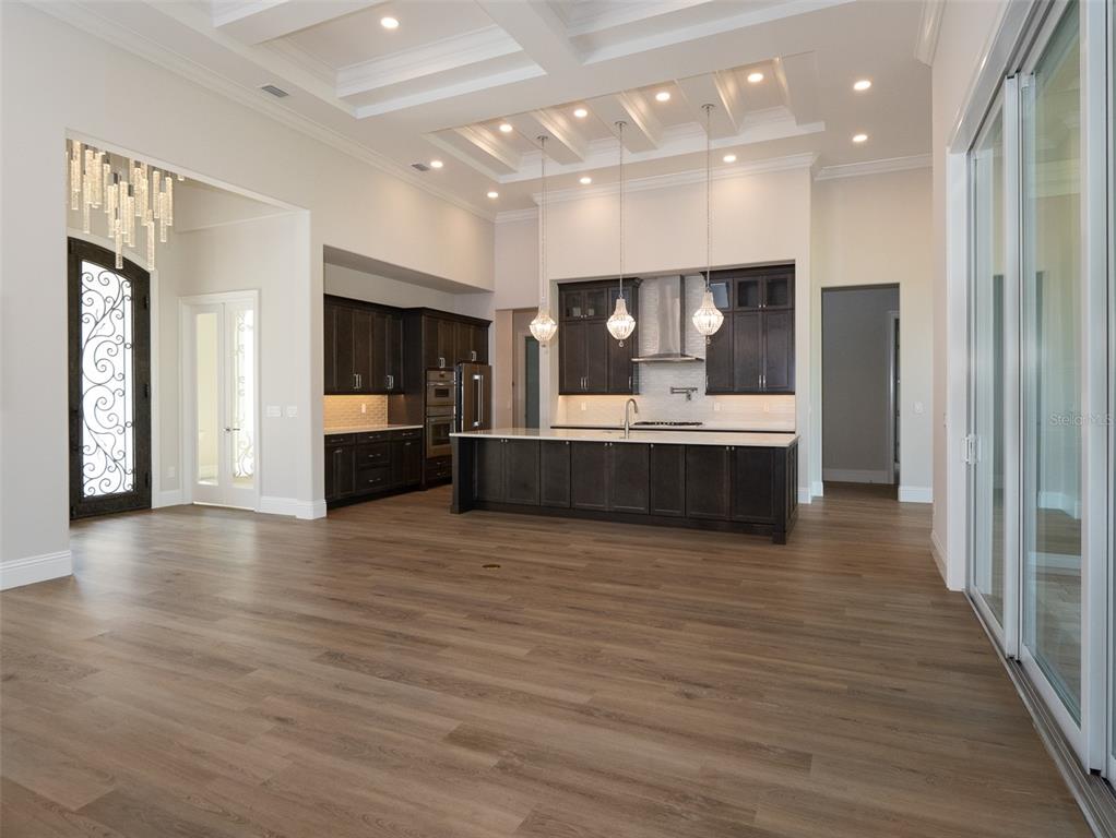 A modern kitchen features dark cabinetry, a large island, and pendant lighting under coffered ceilings — 7647 NW 33RD PLACE, OCALA, FL