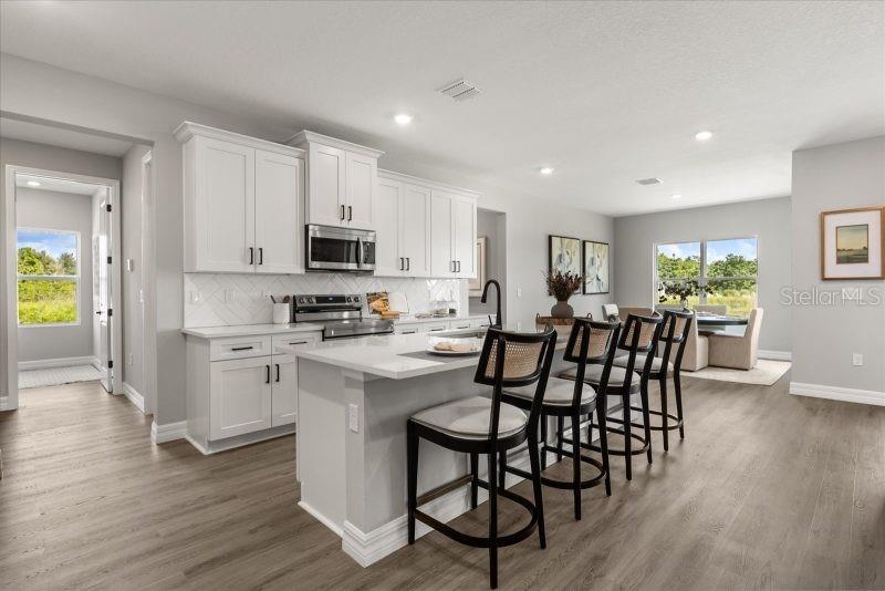 A modern kitchen features white cabinetry, a central island with bar stools, and wood flooring — 10121 SW 45TH AVENUE, OCALA, FL