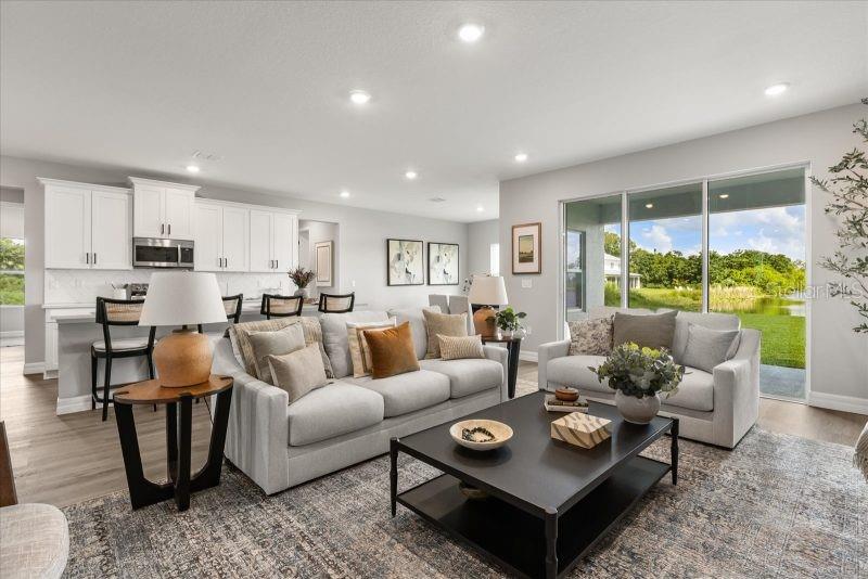 A living room with light gray walls, a sectional sofa, and a kitchen in the background — 10121 SW 45TH AVENUE, OCALA, FL