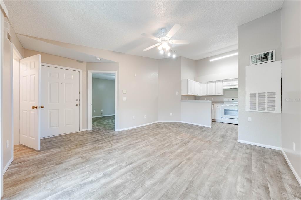 A living room with light wood-look flooring, a ceiling fan, and an adjacent kitchen area — 2210 YANKEE PLACE UNIT 334, ORLANDO, FL