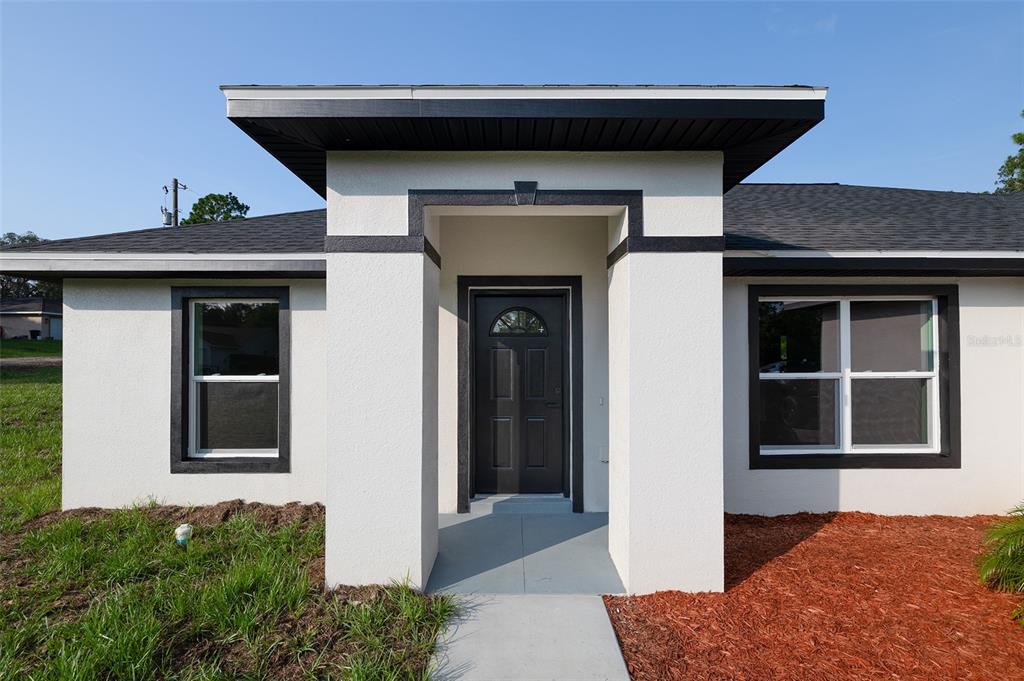 A front view of a white house with a black-trimmed entryway and dark roof shingles — 2902 W EDISON PLACE, DUNNELLON, FL