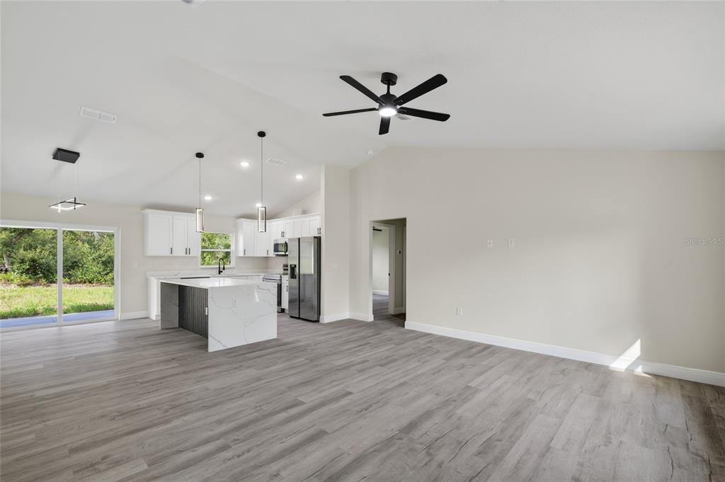 An open-concept kitchen and living area features white cabinetry, a marble-topped island, and wood-look flooring — 2902 W EDISON PLACE, DUNNELLON, FL