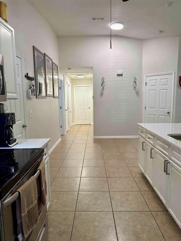 A kitchen with white cabinets and tile flooring leads into a hallway with multiple doors — 313 OAK STREET, AUBURNDALE, FL