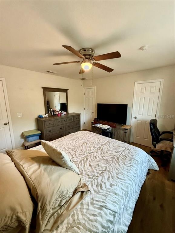 A bedroom features a bed, a dresser with a mirror, a television, and a ceiling fan — 313 OAK STREET, AUBURNDALE, FL