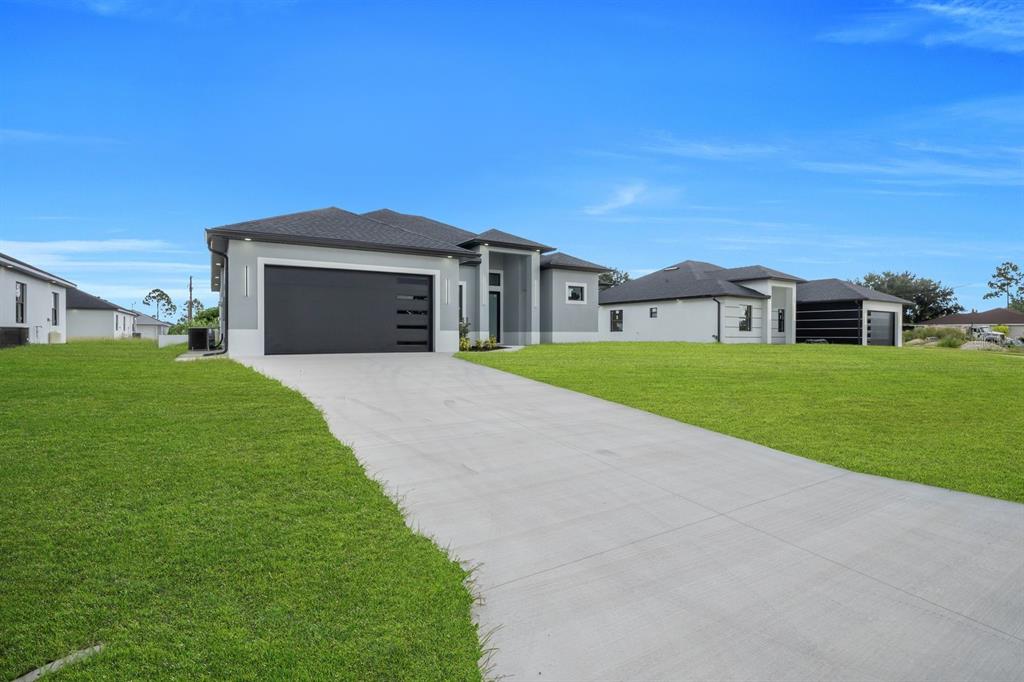 A modern gray single-story house with a black garage door and a concrete driveway — 3616 6TH STREET SW, LEHIGH ACRES, FL