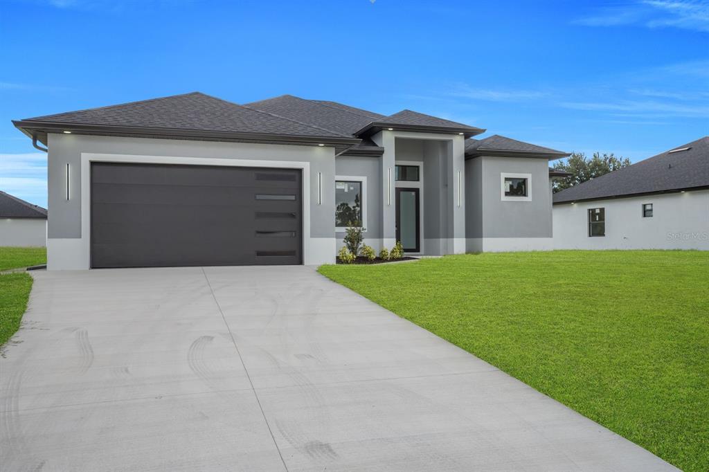 A modern, single-story gray house with a dark garage door and a concrete driveway — 3616 6TH STREET SW, LEHIGH ACRES, FL