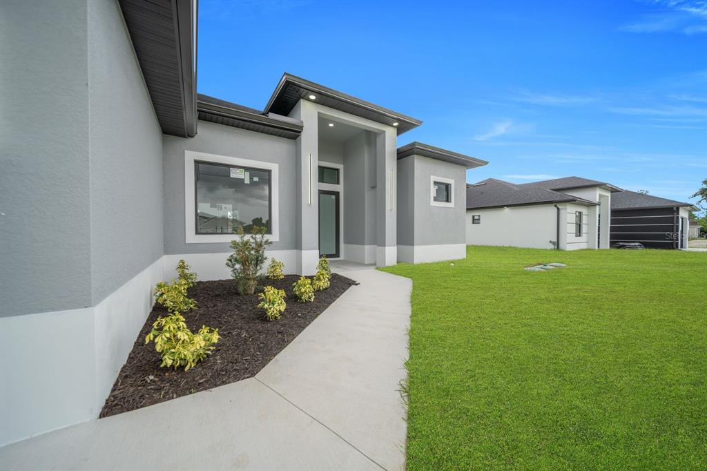 A modern gray stucco house exterior features a concrete walkway leading to the front entrance — 3616 6TH STREET SW, LEHIGH ACRES, FL