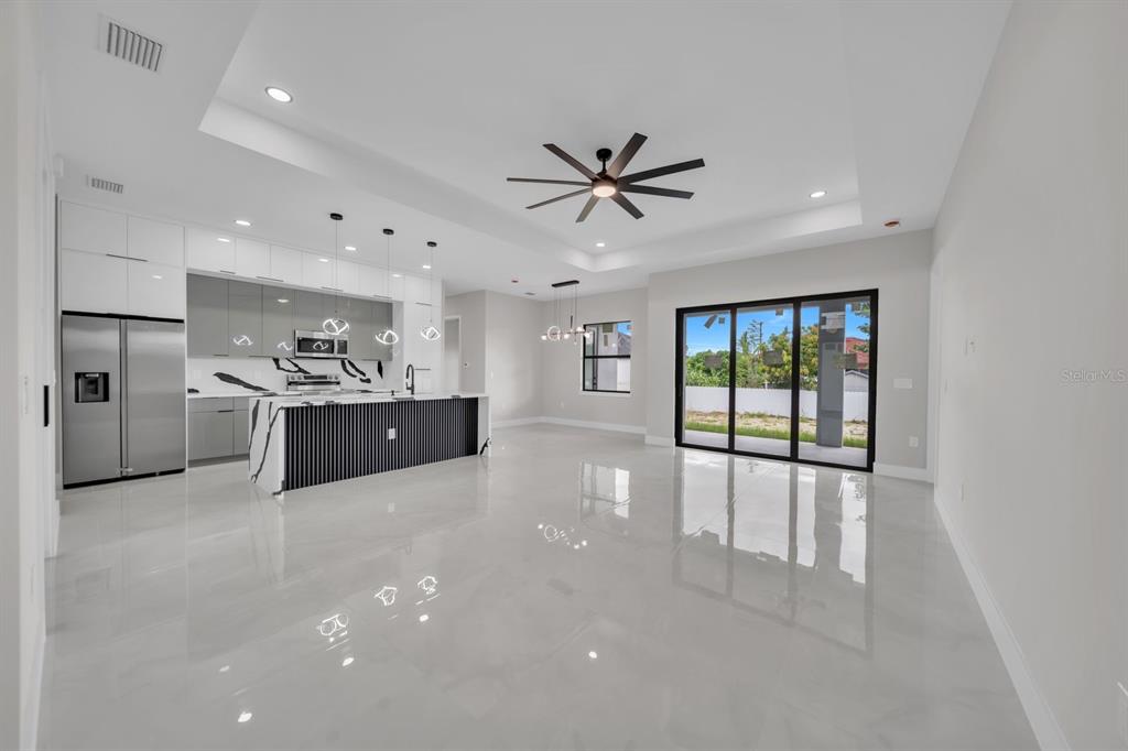 A modern open-concept kitchen and living area with white tile floors and a black island — 3616 6TH STREET SW, LEHIGH ACRES, FL