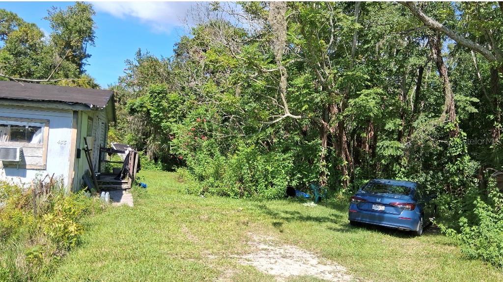 A blue sedan is parked on a grassy lot next to a small, weathered house — 438 N STATE ROAD 415, OSTEEN, FL