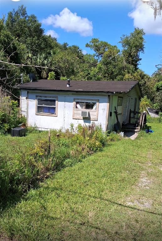 A small, weathered, single-story house with light-colored siding stands in a grassy, overgrown yard — 438 N STATE ROAD 415, OSTEEN, FL