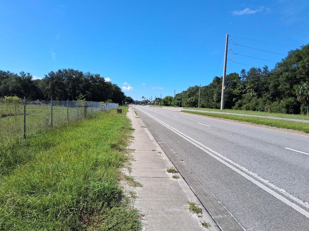 A paved road runs alongside a grassy area bordered by a chain-link fence — 438 N STATE ROAD 415, OSTEEN, FL