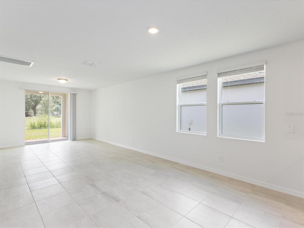 A bright, empty room features white walls, light-colored tile flooring, two windows, and sliding glass doors — 2880 WILD OLIVE DRIVE, ST CLOUD, FL