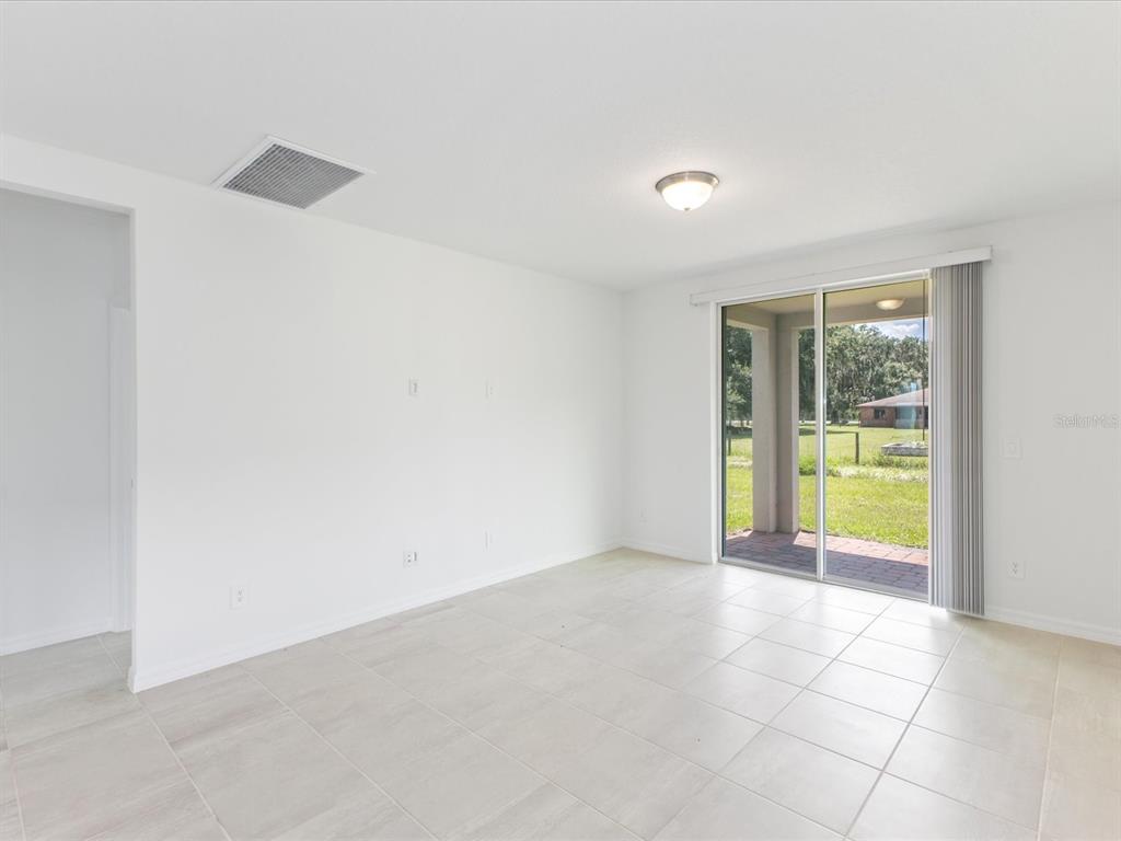 A bright room with white walls, light tile flooring, and sliding glass doors to a patio — 2880 WILD OLIVE DRIVE, ST CLOUD, FL